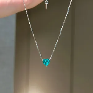 Nahaufnahme einer silbernen Halskette mit einem funkelnden blaugrünen Herz-Zirkon
