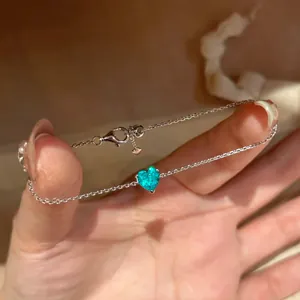 Nahaufnahme eines silbernen Armbands mit einem funkelnden türkisfarbenen Herz-Zirkon.
