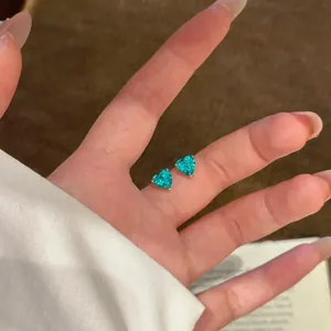 Detailaufnahme von leuchtend türkisfarbenen Zirkonia-Ohrsteckern in Herzform am Finger