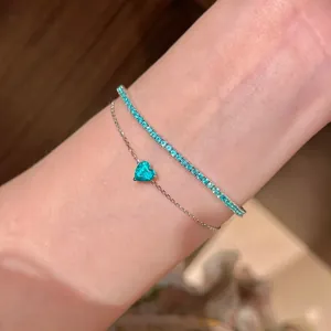 Detail eines eleganten Silberarmbands mit türkisem Herzanhänger und Zirkonsteinen