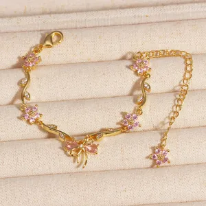 Bracelet chaîne doré exquis avec des fleurs en zircone rose et un délicat charme de nœud