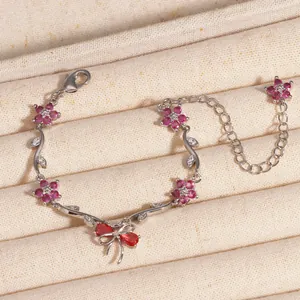 Détail du bracelet avec nœud en zircon, fleurs roses et chaîne à motif de feuilles.
