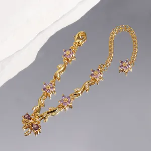 Détail d'un bracelet doré avec des fleurs en zircon violet et un charm de nœud