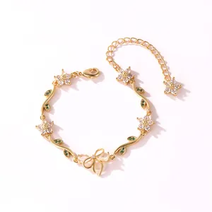 Vue détaillée d'un bracelet en or avec fleurs en zircon, feuilles vertes et nœud.
