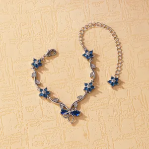 Vue détaillée d'un bracelet argenté avec des breloques papillon et fleurs en zircon bleu.