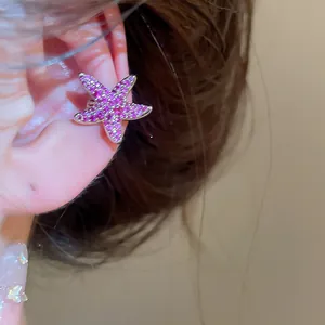 Close-up of a sparkling pink zircon starfish ear cuff worn on a delicate ear
