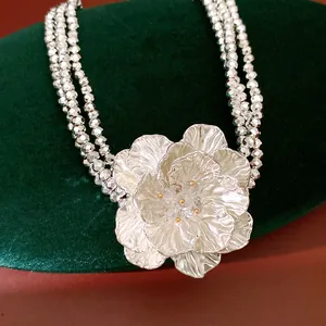 Macro view of multi-layer silver beaded necklace featuring a large ornate flower pendant