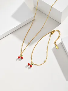 Detail shot of 18K gold plated necklace and bracelet set with red cherry pendants and zircons.