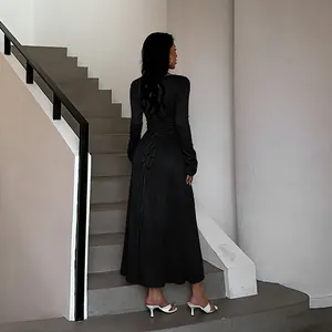 Elegant black long-sleeve maxi dress with back tie-up detail shown on modern stairs