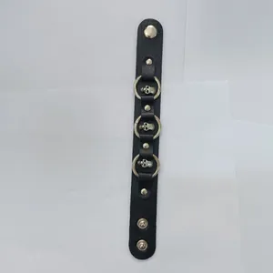 Detail view of a black punk leather bracelet with silver skull charms and rings.