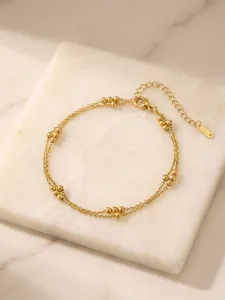 Close-up detail of double-layered gold stainless steel bead bracelet on white marble
