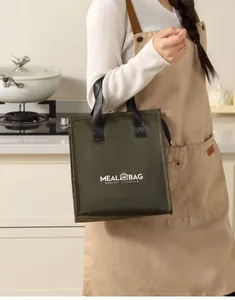 Insulated dark green meal bag with black handles held by a woman in a kitchen setting