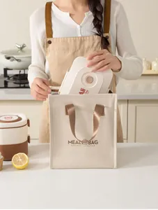 Detail of cream insulated lunch bag being packed with a lunch box in a kitchen.