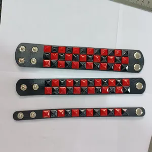 Detail view of three punk leather bracelets with red and black square studs in various widths.