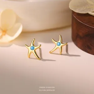 Exquisite macro shot showing the golden starfish stud earrings with a tiny blue stone center