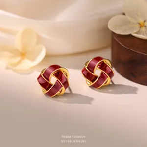 Detailed view of red and gold enamel knot stud earrings on an elegant beige background.