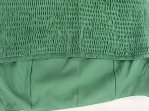 Detailed macro view showing smocking texture on a green elegant halter backless dress fabric.