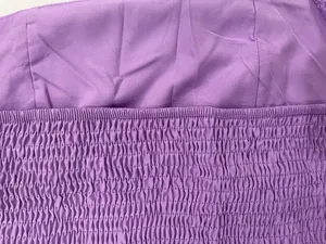 Detailed close-up of purple smocked fabric on a women's halter backless dress, showing texture.