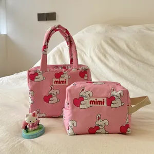 Close-up of pink rabbit print handbag and matching storage pouch on a soft white bed