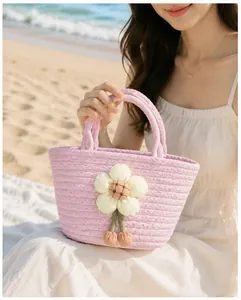 Close-up of a pink hand-woven cotton rope basket bag held by a model on a beach.