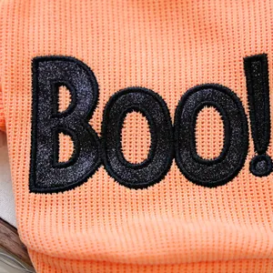 Close-up detail of orange knit Halloween pet sweatshirt with black glitter Boo! embroidery