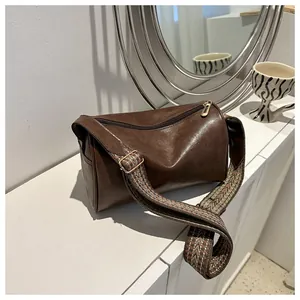 Brown leather pillow bag with a patterned wide strap displayed on a white sideboard.