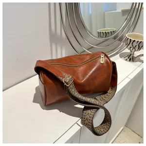 Close-up of a vintage brown leather pillow bag featuring a stylish wide patterned woven strap