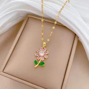 Gros plan d'un collier en acier titane doré orné d'un pendentif fleur en zircon rose et vert.