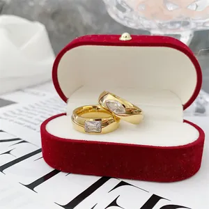 Detail view of two gold titanium steel rings with inset clear stones in a red velvet box.