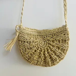 Detailed texture of hand-woven straw crossbody bag with tassel for beach vacation.