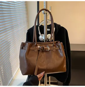 Detailed view of large brown shoulder bag with decorative buckle and long handles