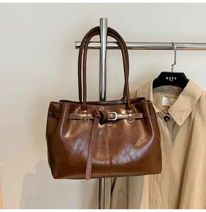 Detailed view of a brown glossy leather underarm bag on a hanger with a trench coat