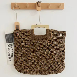 Handgefertigte gewebte Strohhandtasche mit quadratischem Holzgriff an Wandregal