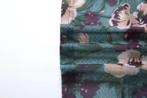 Macro-opname van bloemenstof met hoogwaardige stiksels op een groenblauwe jurk.