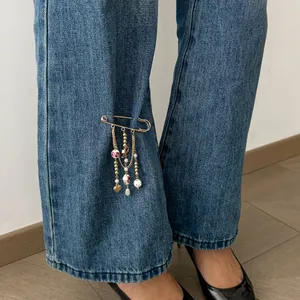 Detailed view of a gold safety pin brooch with floral beads and heart charm on denim