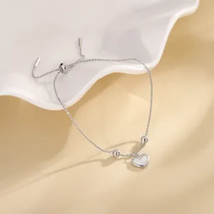 Close-up of heart charm bracelet with adjustable sliding bead and shell inlay details.