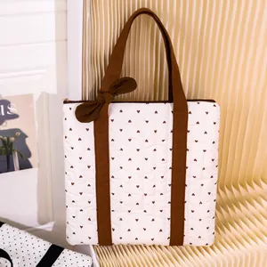 Quilted tote bag with brown heart patterns and bow detail on the strap