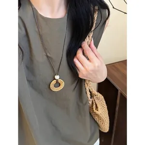 Vista dettagliata di una collana con ciondolo in rattan intrecciato su un outfit casual