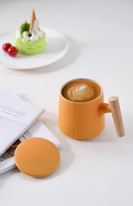 Detail of matte orange ceramic mug with ergonomic wooden handle and matching lid