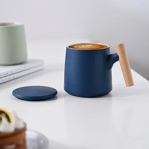 Minimalist matte blue ceramic mug with natural wooden handle and lid on white desk