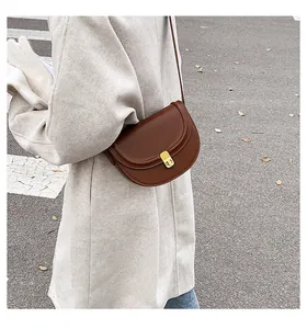 Model wearing a vintage brown leather saddle bag with gold clasp on a beige coat