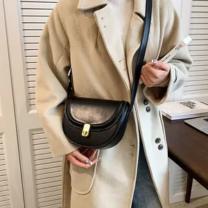 Minimalist black retro saddle bag with gold clasp worn as a stylish crossbody bag
