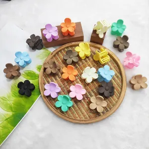 A collection of colorful matte flower-shaped hair claw clips on a rustic woven tray