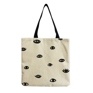 Detail of a canvas tote bag featuring a minimalist black ink-style eye pattern print.