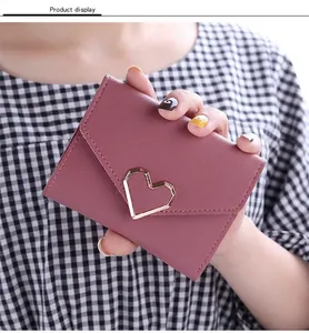 Close-up detail of a dusty rose tri-fold women's wallet featuring a gold heart buckle