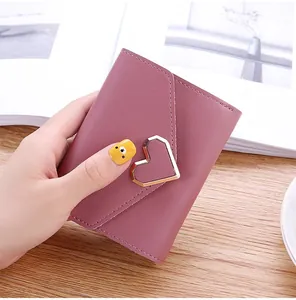 Close-up of small mauve pink three-fold wallet featuring a metallic gold heart-shaped clasp