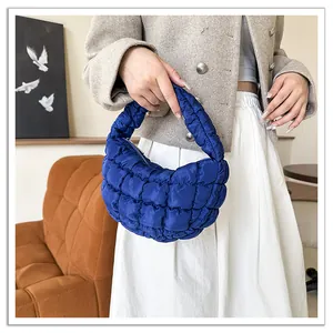 Close-up view of a vibrant blue quilted cloud handbag with padded texture held by a model.
