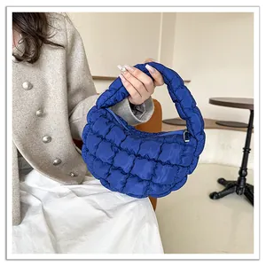 Close-up of a royal blue quilted puffy cloud bag held by a person in a stylish cafe