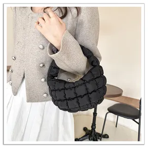 Detailed view of a black quilted cloud bag held by a model wearing a grey blazer