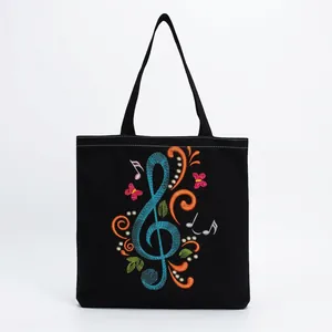 Close-up of black canvas tote bag with colorful musical note and butterfly embroidery.